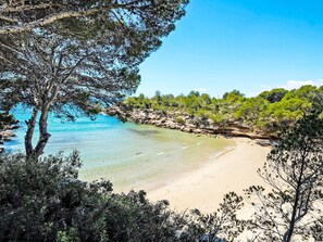 A beach with clear turquoise water, sandy shore, and surrounding greenery.