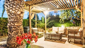 Ein Außenbereich mit Terrassenausstattung, Korbmöbeln, einer Steinsäule und einer Pergola.