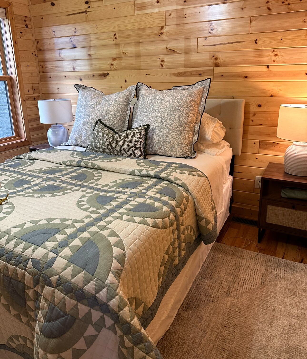 Quarto com painéis de madeira, uma cama, almofadas, mesa de cabeceira e abajur.