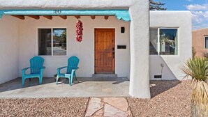 Un bâtiment avec une porte en bois, deux fenêtres et un porche orné de chaises turquoise.