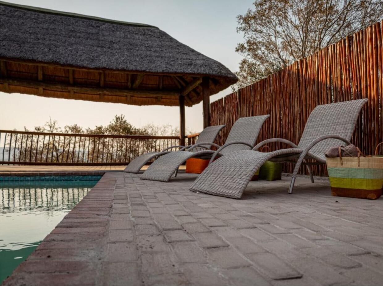 Un espace aménagé au bord de la piscine, avec des chaises longues et une structure dotée d’un toit de chaume.