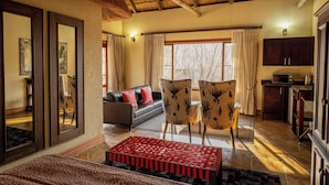 A room with a sofa, two chairs, a red woven bench, a large mirror, and a kitchen area. - Serene Retreat in Bracondale Mountain Views & Private Oasis (Bracondale)