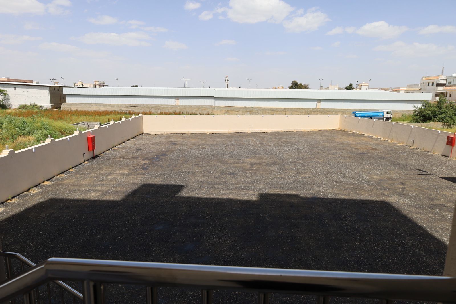 An outdoor parking area with a concrete floor, surrounded by a low wall and a metal railing.