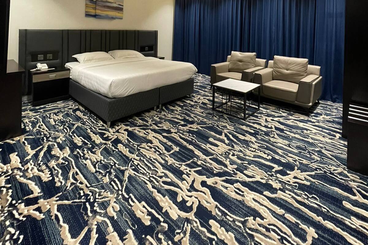 Ein modernes Hotelzimmer mit einem großen Bett, einem Schreibtisch, zwei Sesseln, einem kleinen Tisch und einem blauen Vorhang.