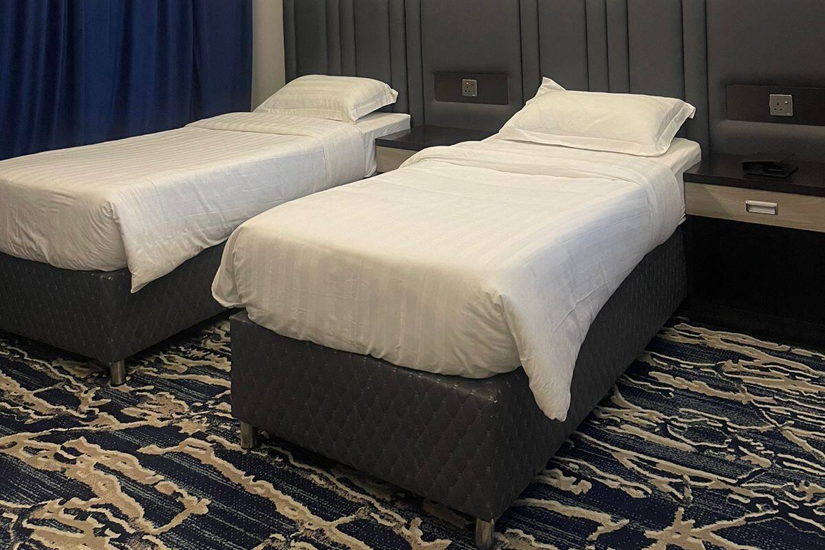 Ein Hotelzimmer mit zwei Betten, einem dunkel gemusterten Teppich und abstrakter Wandkunst.