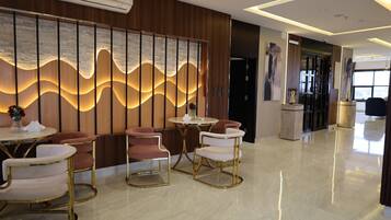Een moderne hotel lobby met een zithoek met ronde tafels en gestoffeerde stoelen, een decoratieve wand met een golfpatroon, en een schone, gepolijste vloer.