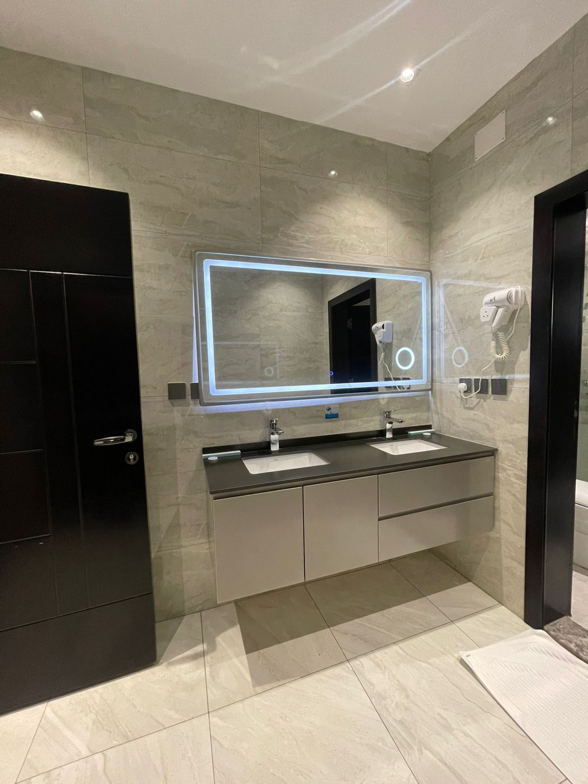 Un baño moderno con un espejo grande, dos lavamanos y un secador de pelo en la pared.