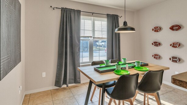 Un comedor con una mesa dispuesta para cuatro personas, una lámpara colgante y una ventana con cortinas.