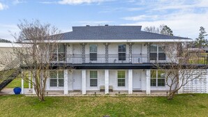 Een woonhuis met twee verdiepingen, een balkon, een overdekte veranda en een verzorgd gazon.