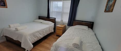 A bedroom with two beds, a nightstand, a ceiling fan, and a window with curtains.
