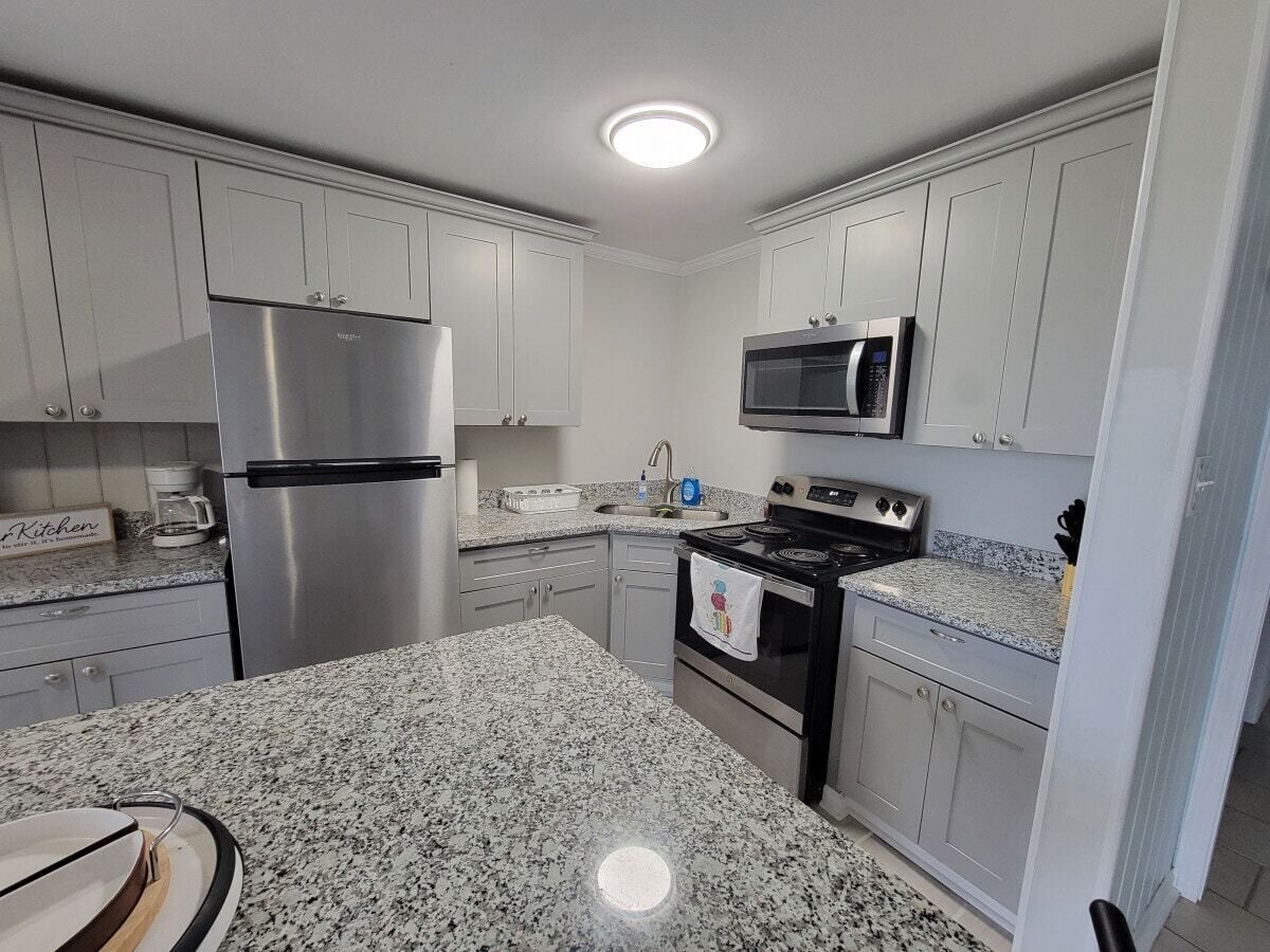 A kitchen with white cabinets, a stainless steel refrigerator, a microwave, and a stove.