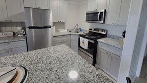 Una cocina con armarios blancos, un refrigerador de acero inoxidable, un microondas y una estufa.