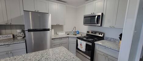 A kitchen with white cabinets, a stainless steel refrigerator, a microwave, and a stove.