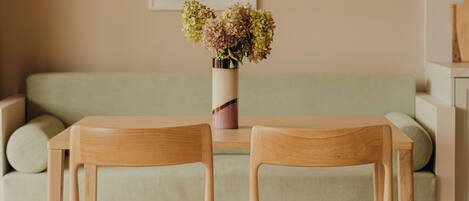 Un comedor con dos sillas de madera, una mesa, una lámpara colgante y un sofá.