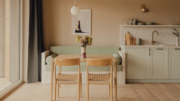 Una cocina moderna con armarios de madera, una mesa de comedor con sillas, una lámpara colgante y un ventanal con cortinas.