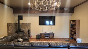 A living room with a stone wall, a fireplace, a leather sofa, a television, and a wooden bookshelf. - The Treehouse a 4-bedroom log cabin on 3 acres in Heber-Overgaard (Heber-Overgaard)