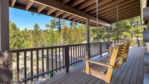 A wooden deck with a swing chair, a railing, and a view of trees and buildings. - The Treehouse a 4-bedroom log cabin on 3 acres in Heber-Overgaard (Heber-Overgaard)