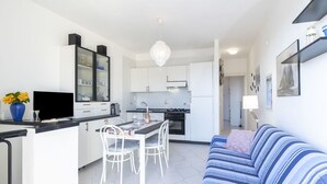 Eine moderne Küche mit weißen Schränken, ein Essbereich mit Tisch und Stühlen sowie ein Wohnzimmer mit gestreifter Couch.