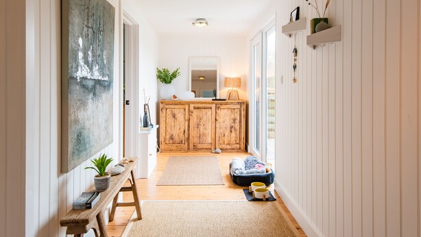 Un couloir avec un banc en bois, un grand tableau abstrait, une armoire et un petit tapis.