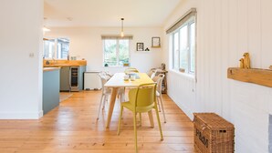 Une cuisine lumineuse avec un plancher en bois, une table à manger jaune et une fenêtre donnant sur un paysage verdoyant.