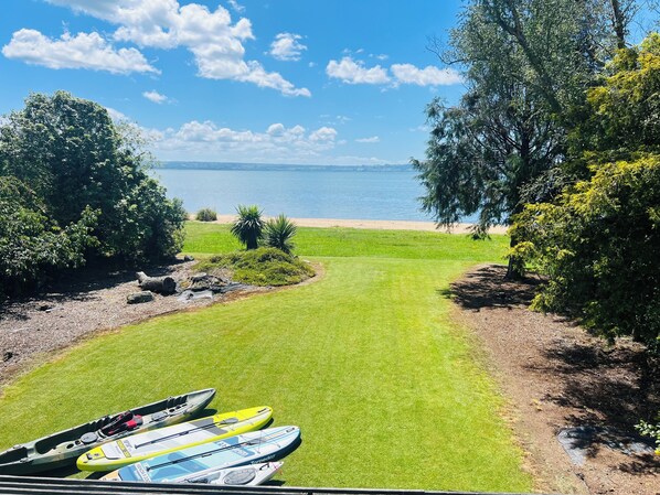 A grassy area with kayaks, a beach, and a lake under a clear sky. - Tranquil Lake Side Retreat: Your Perfect Getaway In Holdens Bay (Holdens Bay)