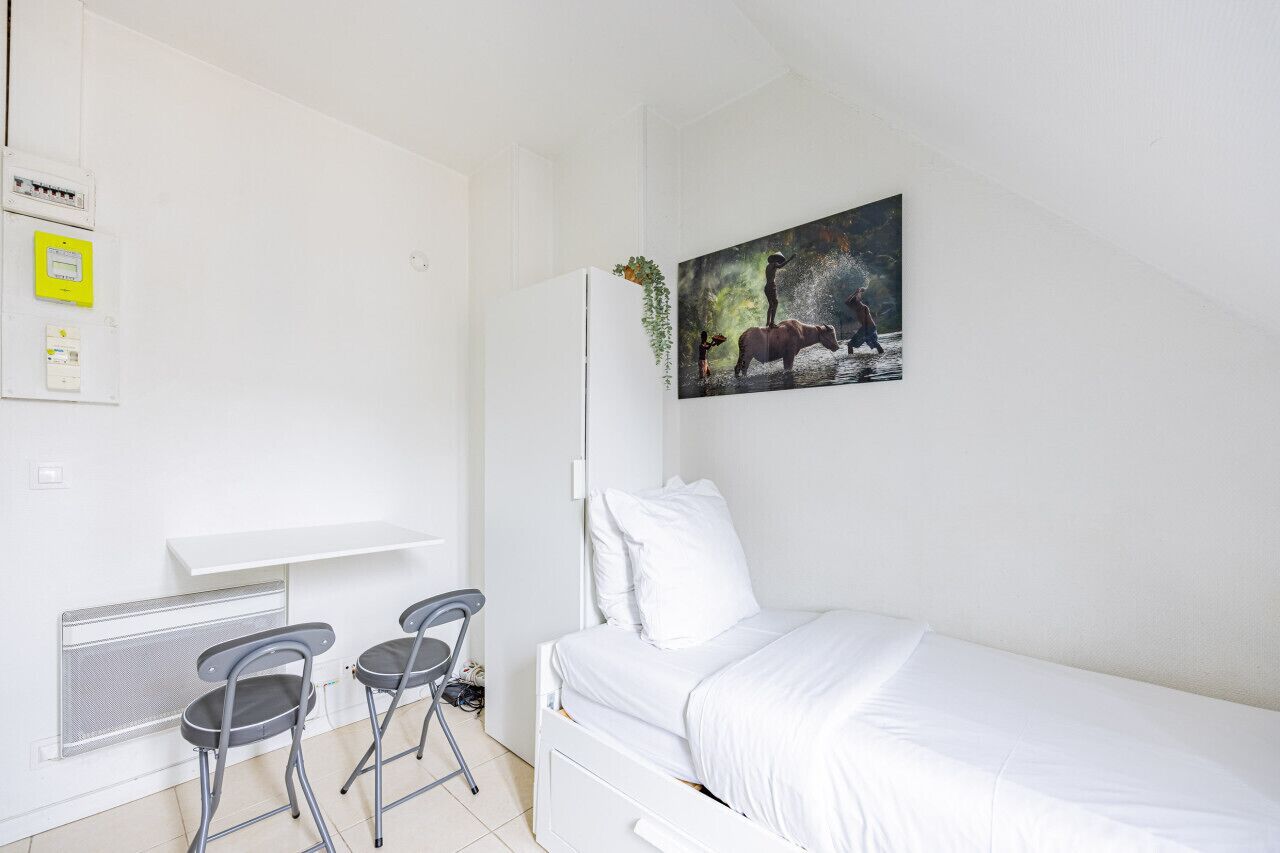 Une chambre à coucher moderne avec un lit, un bureau, deux chaises et un tableau au mur.