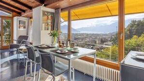 Un espace repas moderne avec une table en verre, des chaises en métal et une vue sur le paysage urbain et les montagnes.
