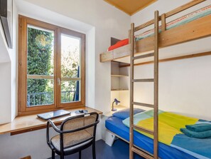 A bunk bed with a desk and chair, a window with a view of greenery, and a lamp on the desk. - Egner- Apt.Caretta by Interhome (Locarno)