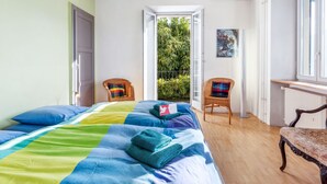 Une chambre à coucher avec un lit, deux fauteuils en osier, une fenêtre et un radiateur.