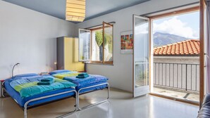 Et moderne soveværelse med seng, senget lampe, garderobe og balkon med udsigt til bjerge.