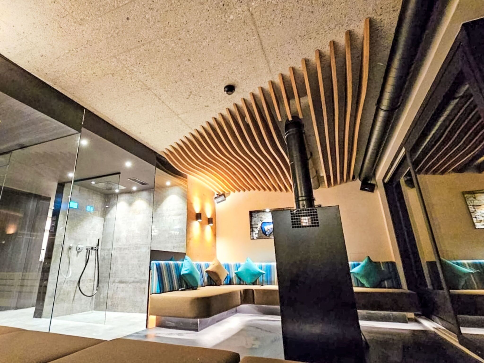 Ein moderner Wellnessbereich mit einer gläsernen Dusche, einer Sitzecke mit Kissen und einer schwarzen Säule.
