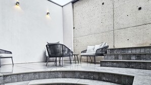 A modern outdoor seating area with tiered stone steps, two lounge chairs, and a wall-mounted light fixture.