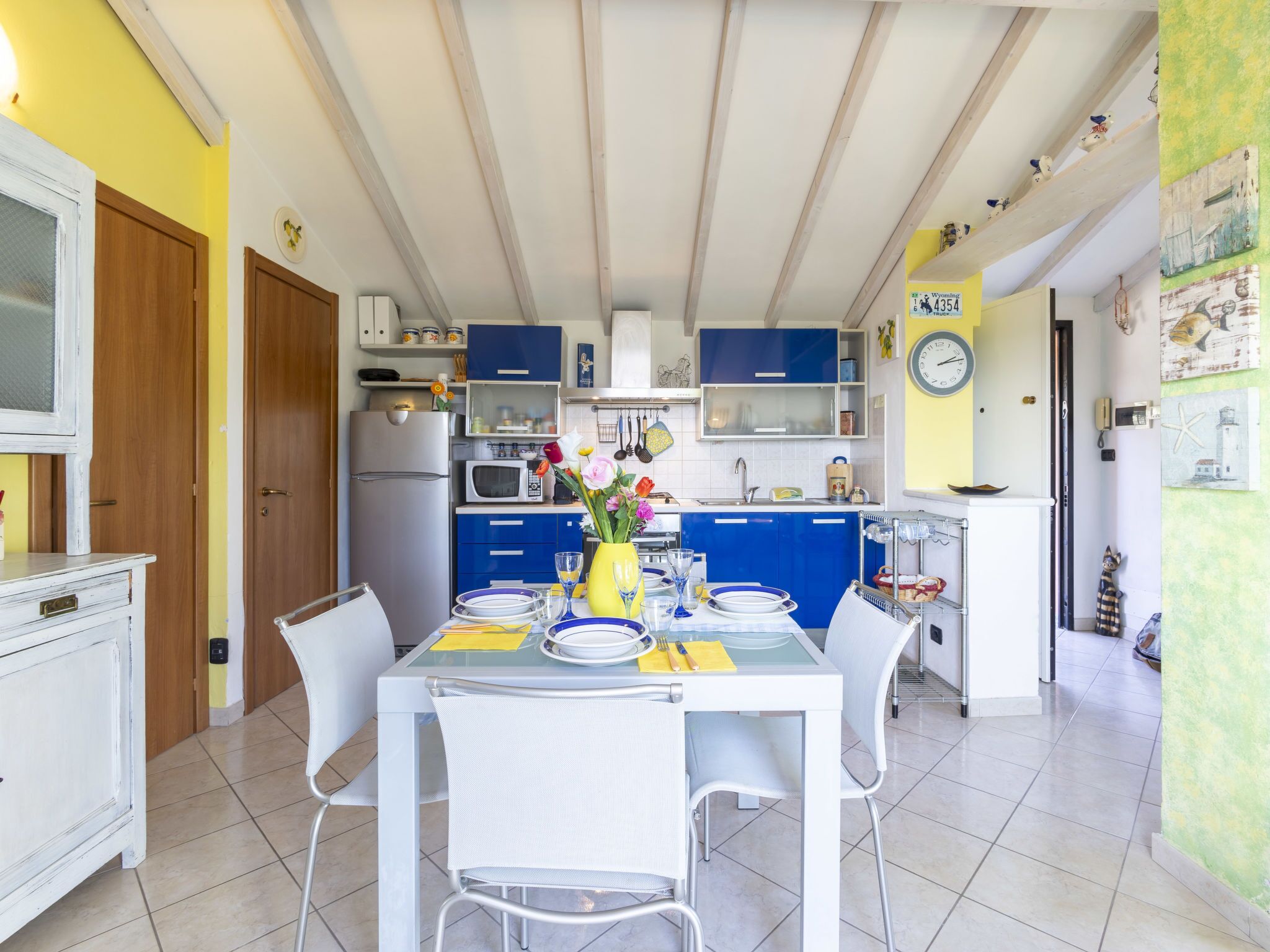 A compact kitchen with blue cabinets, a white refrigerator, and a dining table set for four.