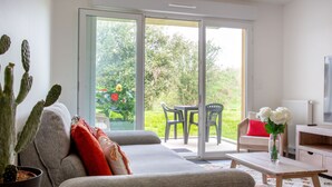 A modern living room with a grey sofa, a cactus plant, and a view of a garden through large sliding glass doors. - Atlantica by Interhome (Pornic)