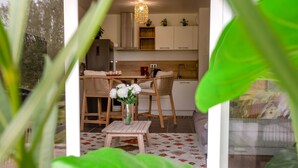 A modern kitchen with white cabinets, a wooden dining table, and chairs. There is a small table with a vase of flowers in the foreground. - Atlantica by Interhome (Pornic)