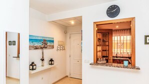 Un couloir avec une horloge, un tableau, un miroir et une fenêtre donnant sur une pièce.