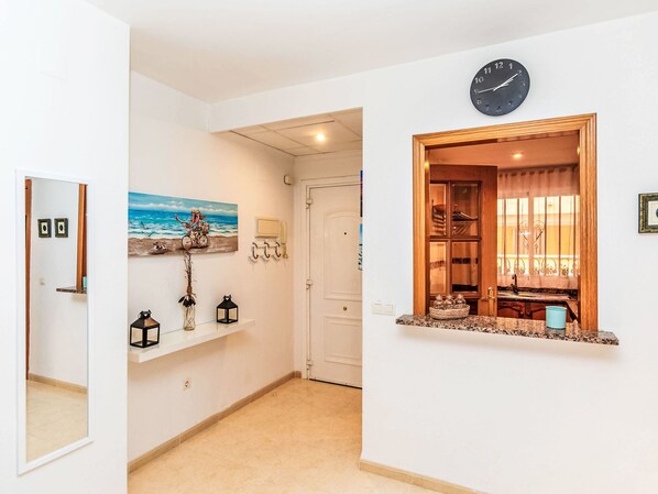 Un couloir avec une horloge, un tableau, un miroir et une fenêtre donnant sur une pièce.