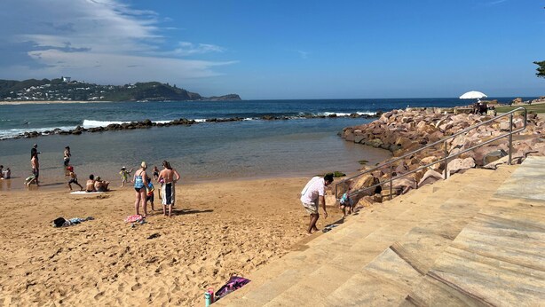 A beach with rocky terrain, a clear sky, and a distant view of a town.