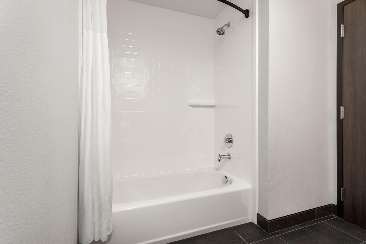 A modern shower enclosure with a white tiled wall, a showerhead, and a control panel.