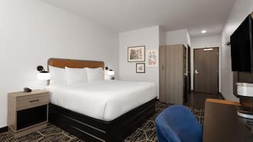 A hotel room with a bed, bedside table, lamp, and a TV.