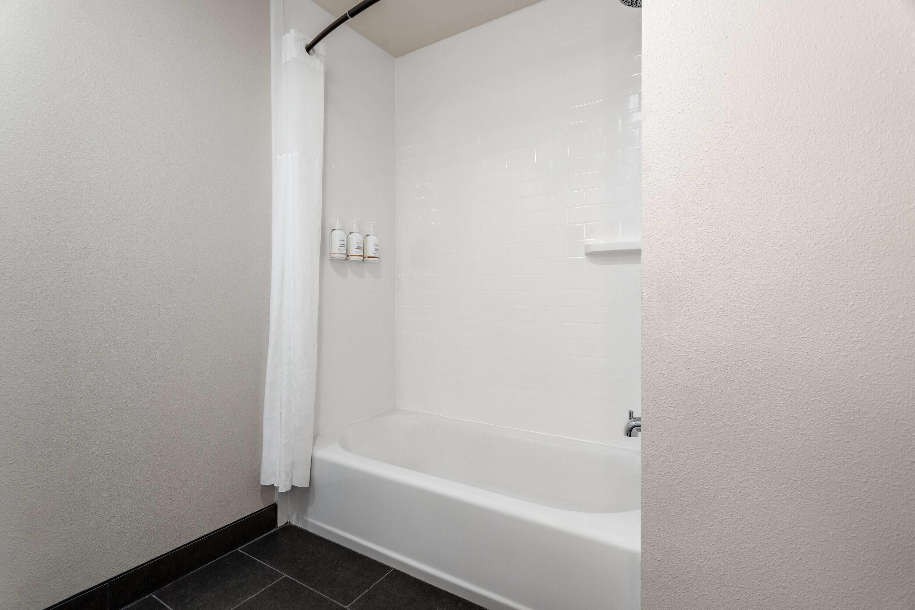Un baño con una bañera blanca, una cortina de ducha y tres botellas de artículos de aseo en la pared.