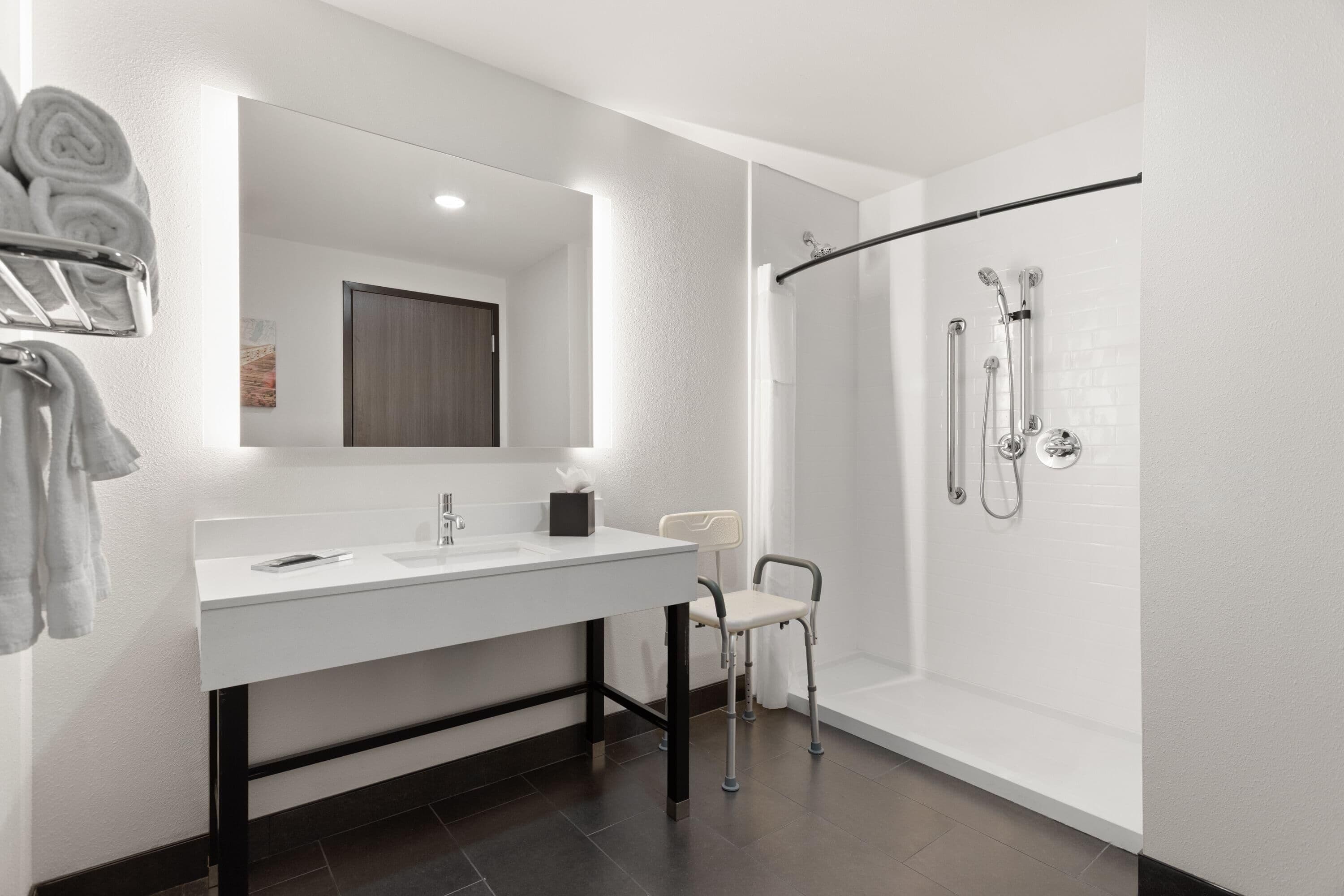 A modern bathroom with a white vanity, a large mirror, a shower with a glass door, and a towel rack with towels.