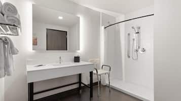 A modern bathroom with a white vanity, a large mirror, a shower with a glass door, and a towel rack with towels.
