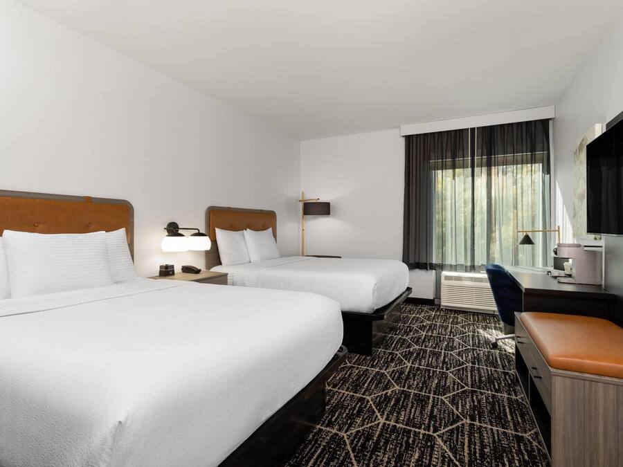 A hotel room with two beds, a desk, a chair, a TV, and a window with curtains.
