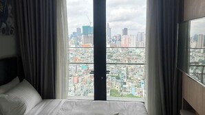 A hotel room with a large bed, a television on the wall, and a city view through the window. - LuSSO Suites - D1mension & Zenity Tower (Ho Chi Minh City)