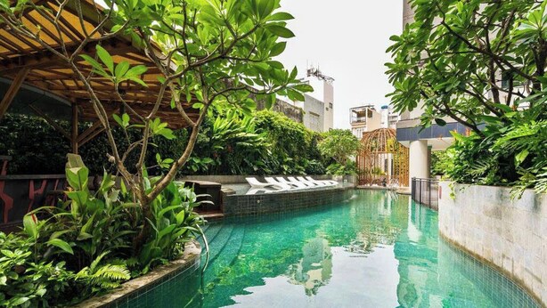 A swimming pool with a tiled edge, surrounded by lush greenery and a wooden pergola. - LuSSO Suites - D1mension & Zenity Tower (Ho Chi Minh City)