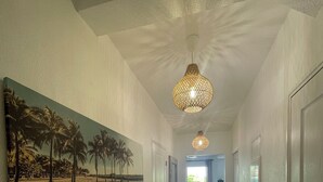A hallway with a bench, a painting of palm trees, and a hanging light fixture.