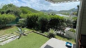 A covered patio with a view of a landscaped garden, a body of water, and distant hills.