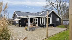 A black house with a wooden deck, a covered patio, and a large window.