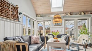 A cozy living room with a sofa, a coffee table, and a rocking chair. There is a large window and a ceiling fan.